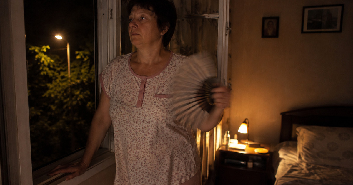 женщина 45+ ночью у открытого окна, обмахивается веером, у кровати горит настольная лампа